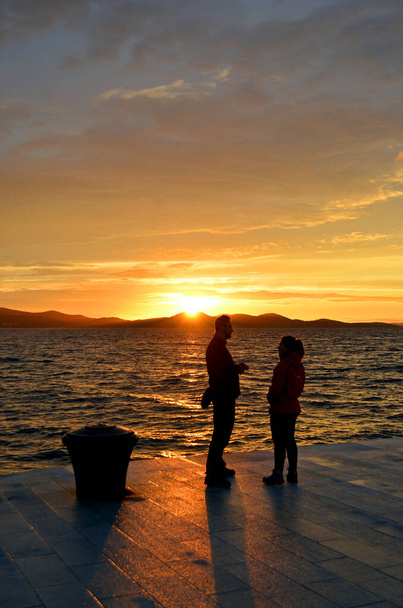 Coucher de soleil (lever du soleil, aube) en mer avec des silhouettes de personnes (couple) à Zadar (Croatie)) - Photo, image