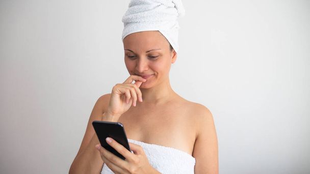 Caucasian woman wrapped in a towels browsing on the phone. Copy space for text. - Foto, imagen