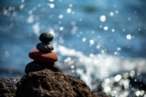 Nahaufnahme von aufeinander gestapelten Kieselsteinen in einem Gleichgewicht mit dem blauen Meer im Hintergrund - Foto, Bild