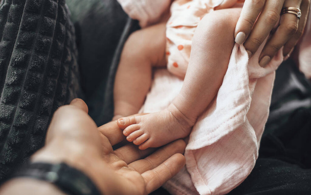 Bovenaanzicht foto van een pasgeboren baby voeten en haar ouders omarmen haar - Foto, afbeelding
