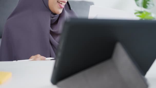 Asia muslim lady wear headphone using tablet talk to colleagues about sale report in conference video call while working from home at living room. Social distancing, quarantine for corona virus. - Filmmaterial, Video