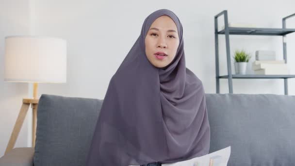Asia muslim lady wear hijab use computer laptop talk to colleagues about sale report in video call meeting while remotely work from home at living room. Social distancing, quarantine for corona virus. - Materiaali, video