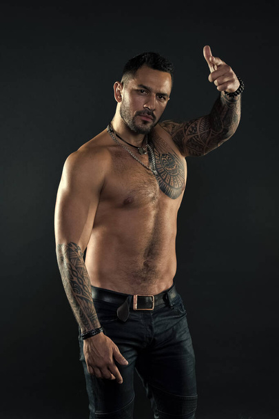 Hey you. Handsome fit tattooed man wear jeans pointing forward. Man handsome shirtless muscular with jeans over dark background. Muscular tattooed athlete look attractive. Sport and fashion concept - Foto, afbeelding