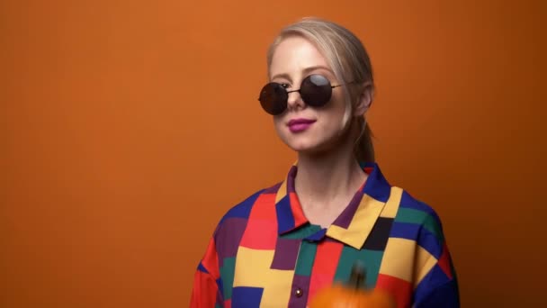 Stil Blondine im 90er Hemd mit Kürbis auf orangefarbenem Hintergrund - Filmmaterial, Video