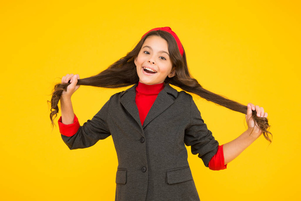 Happy small kid in school uniform hold long brunette hair locks yellow background, salon - Fotografie, Obrázek