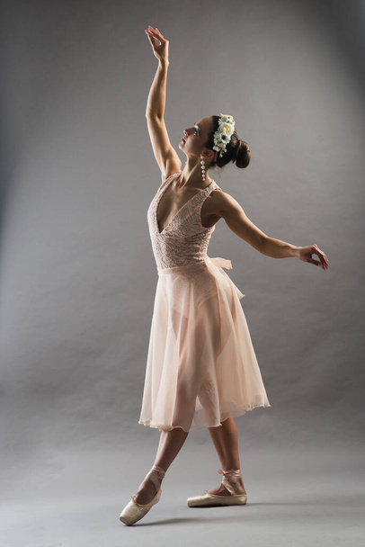 young beautiful ballet dancer in beige swimsuit posing on pointes on light grey studio background - Fotografie, Obrázek