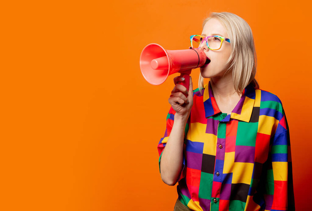 Stile bionda in abiti anni '90 e occhiali arcobaleno con megafono su sfondo arancione - Foto, immagini