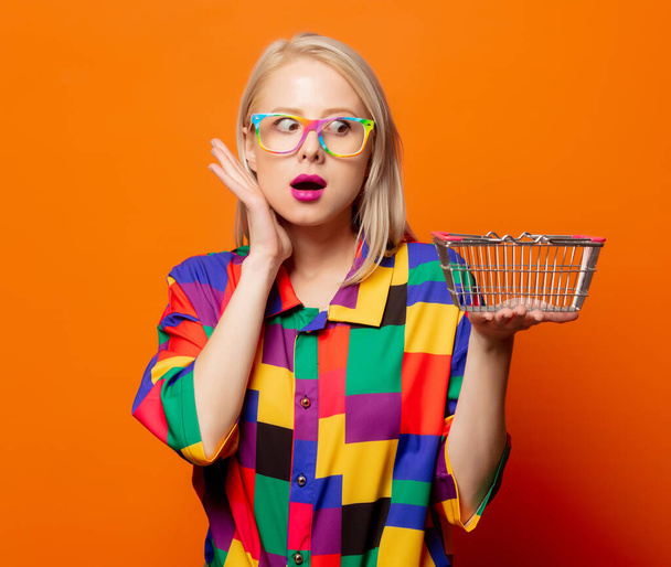 Style blonde in 90s clothes with shoping basket on orange background - Photo, Image