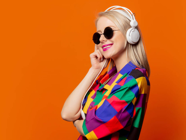 Στυλ ξανθιά σε 90s ρούχα με ακουστικά σε πορτοκαλί φόντο - Φωτογραφία, εικόνα