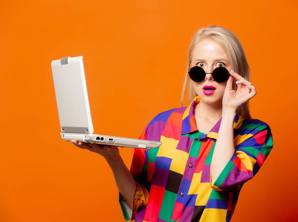 Tyyli blondi 90-luvulla vaatteita kannettavan tietokoneen oranssi tausta - Valokuva, kuva