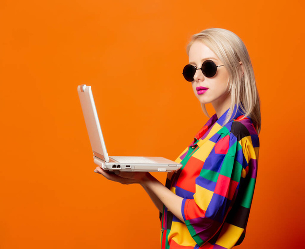 Style blonde in 90s clothes with notebook computer on orange background - Fotó, kép
