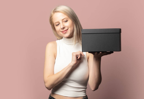 Portrait de blonde en haut avec boîte cadeau noire sur fond rose - Photo, image