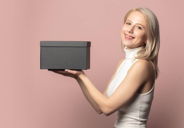 Portrait de blonde en haut avec boîte cadeau noire sur fond rose - Photo, image