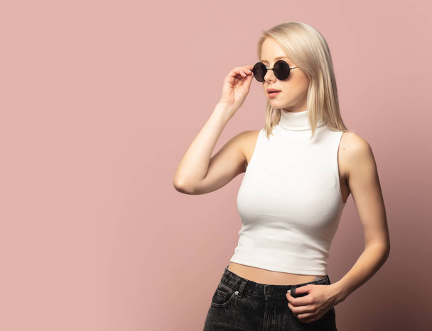 Style blonde en haut et lunettes de soleil sur fond rose - Photo, image