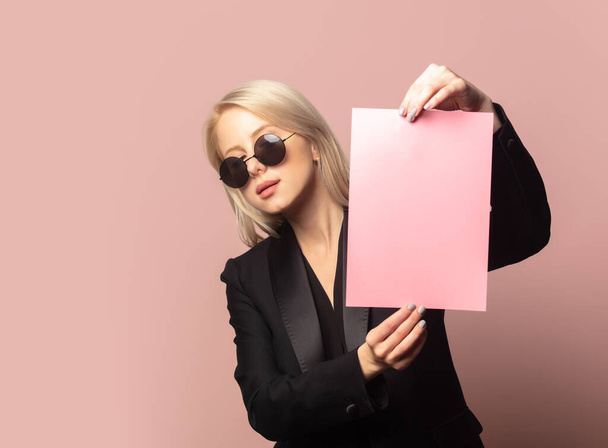 Stylische Blondine in Blazer und Sonnenbrille mit Papier auf rosa Hintergrund - Foto, Bild