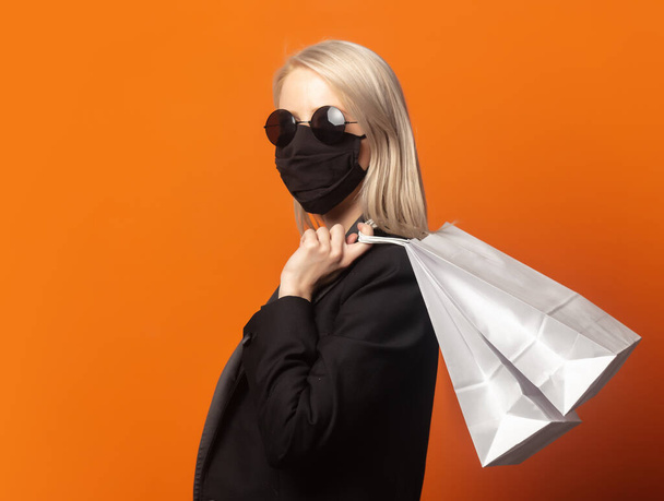 Style blonde in black blazer with shopping bags on an exuberant orange background - Photo, Image