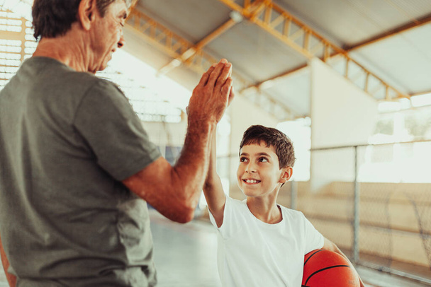Latin grandfather and grandson playing basketball on the court - 写真・画像