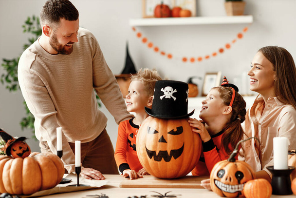 Wesoły ojciec rodziny, matka i dzieci sprawia, że Jack o latarnia z dyni i dekoruje dom podczas zbierania się wokół stołu w przytulnej kuchni podczas obchodów Halloween w Hom - Zdjęcie, obraz