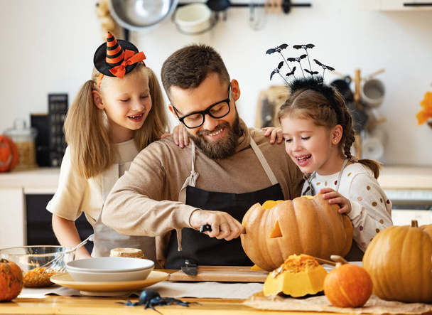 glücklicher Familienvater und seine Töchter bereiten sich zu Hause in der Küche auf Halloween vor, indem sie Kürbisse schnitzen - Foto, Bild