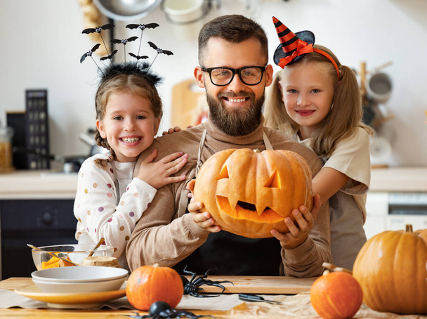 szczęśliwy ojciec rodziny i dzieci córki przygotować się na Halloween rzeźbiąc dynie w domu w kuchni - Zdjęcie, obraz