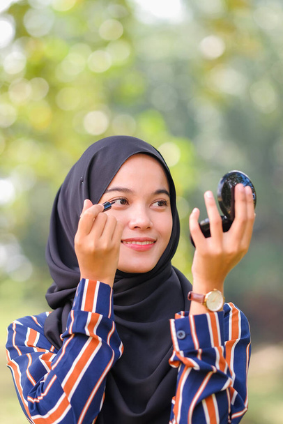 Gyönyörű muszlim lány fekete hidzsáb alkalmazó smink segítségével szemceruza és nézi a tükörbe - Fotó, kép