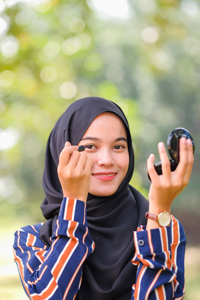 Όμορφη μουσουλμάνα κοπέλα σε μαύρο χιτζάμπ εφαρμογή μακιγιάζ χρησιμοποιώντας eyeliner και κοιτάζοντας κάμερα - Φωτογραφία, εικόνα