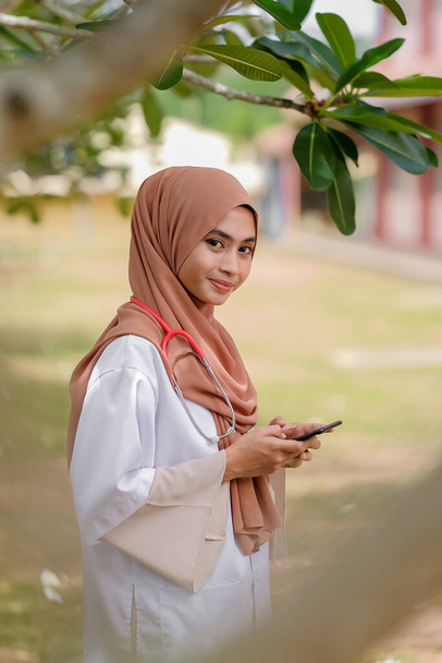 Veterinaria musulmana che tiene uno smartphone nel giardino dell'ospedale. Concetto di servizio medico e sanitario. - Foto, immagini