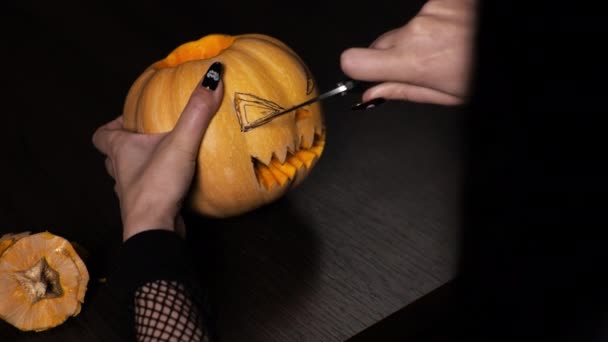 Young woman prepares a pumpkin for Halloween. Cuts out the eyes. Celebration - Materiaali, video