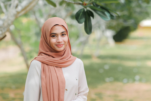 Pretty muslim female standing under a tree with smiles. - Photo, Image