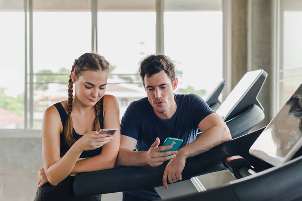 Couples exercise at the gym. Couple having fun playing with smartphones Near the exercise machine. - Foto, Imagen