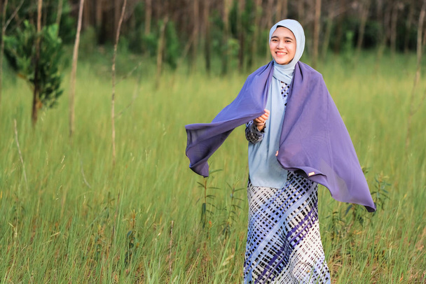 Portrét šťastného krásného mladého modelu v módním hidžábském stylu pózujícího v zelené oblasti při držení látky. Stylový muslimská žena hidžáb módní životní styl portrét koncept. - Fotografie, Obrázek