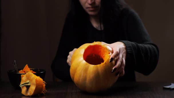 Young brunette woman carves a pumpkin for Halloween Preparation for the holiday - Felvétel, videó