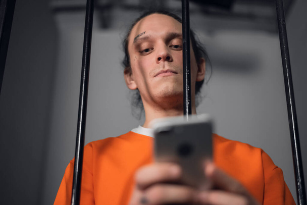 刑務所で彼の顔に入れ墨を持つ危険な犯罪者は、インターネット上でサイバー犯罪を犯すためのスマートフォンを持っています. - 写真・画像