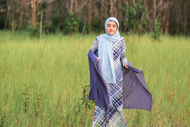 Портрет щасливого молодого зразка в модному стилі хіджабу, який позує в зеленій місцевості, зберігаючи тканину. Стильний мусульманський стиль життя жінки-хіджабу Портрет. - Фото, зображення