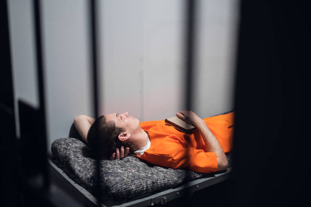 Niebezpieczny więzień w celi spoczywa i śpi w izolatce na pryczy w pomarańczowym szlafroku.. - Zdjęcie, obraz