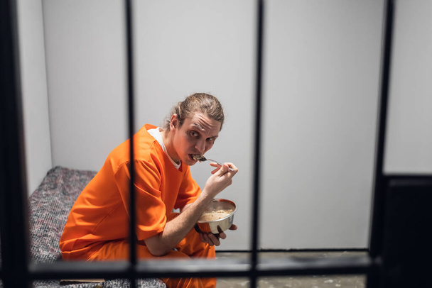 Ужин в тюремной камере. Заключенный ест безвкусную еду из железной чаши под охраной за решеткой. - Фото, изображение