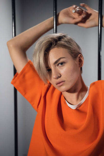 Portrait of a beautiful blonde with short hair on the background of prison bars - Foto, afbeelding