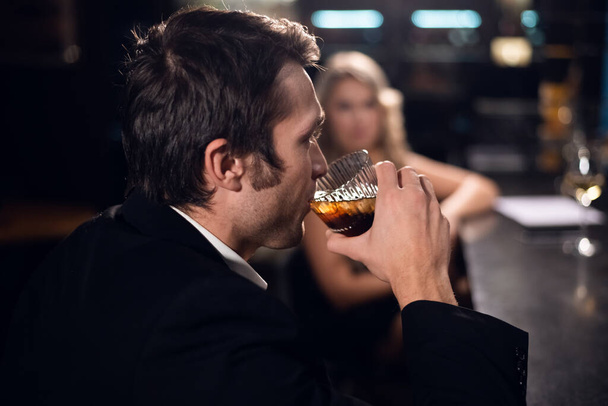 Ένας νεαρός με κουστούμι πίνει ουίσκι με κόκα και πάγο στο μπαρ ενός κλαμπ. - Φωτογραφία, εικόνα