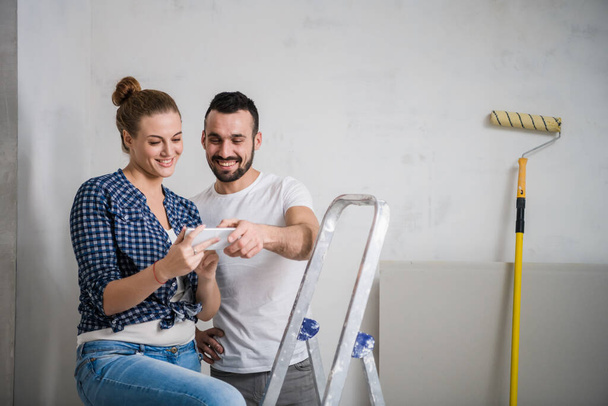 Un homme et une jeune fille regardent une photo sur un smartphone dans un appartement en rénovation - Photo, image