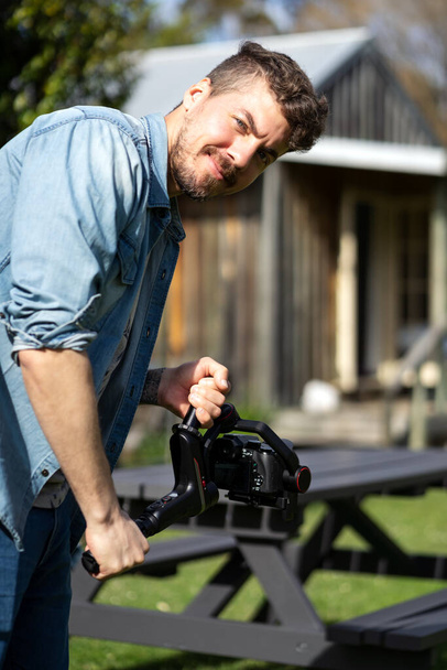Biały mężczyzna trzymający gimbal podczas filmowania na zewnątrz. Fotografia pionowa - Zdjęcie, obraz