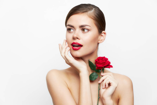 Vrouw met rode bloem houdt zijn hand op zijn gezicht kijken naar de zijkant model heldere make-up  - Foto, afbeelding