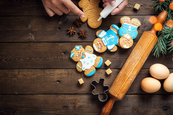 Female hands decorate Christmas cookies on wooden background top view - Fotó, kép