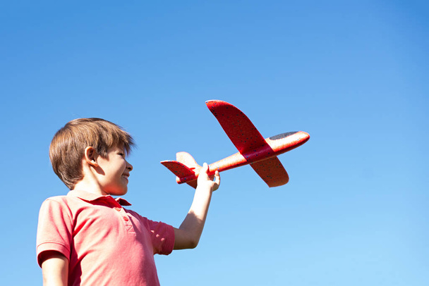 Een jongen die met een rood vliegtuig tegen de lucht speelt. Gelukkige kinderen spelletjes - Foto, afbeelding