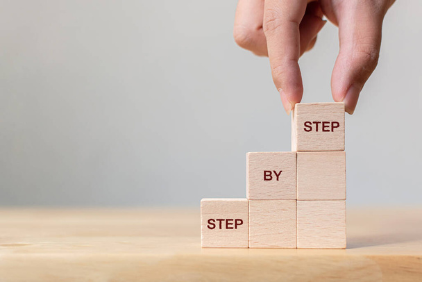 Hand arranging wood block stacking as step stair on top with word Step By Step. Business concept for personal ladder of success process - Photo, Image