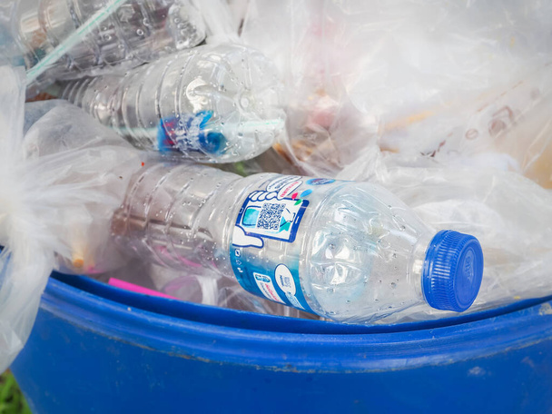 Amnat Charoen, Tailandia - 30 de agosto de 2020: Botellas de agua de plástico transparente, tapas azules y muchos otros tipos de residuos se tiran a los contenedores de color azul claro. - Foto, imagen