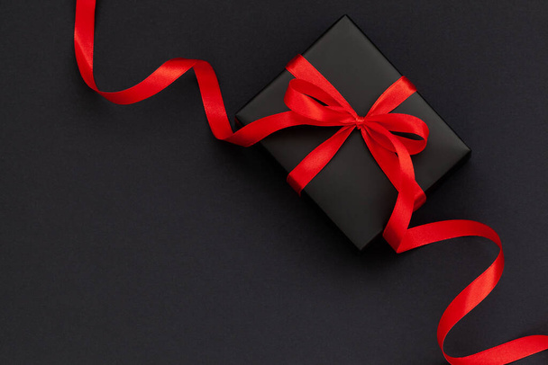 Black Friday concept. Top view of black gift box with red ribbon on black and red background with copy space for text. - Photo, image