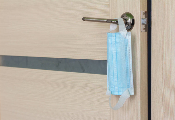 A protective surgical mask hangs on the door handle.Protection from viruses and infections when leaving the house and entering public places. - Photo, Image