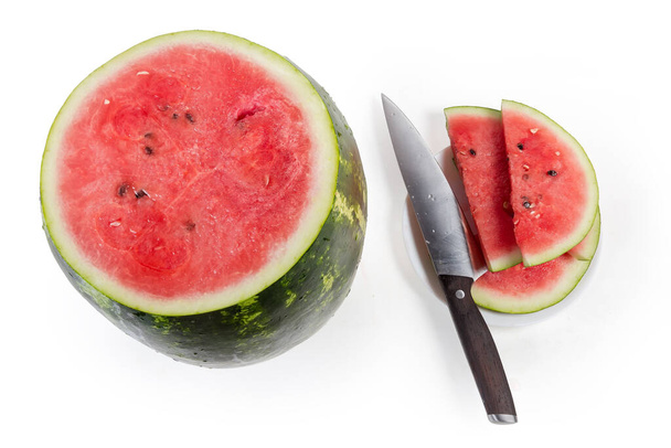 Teilweise in Scheiben geschnittene große dunkelgrün gestreifte Wassermelone und Küchenmesser auf weißem Hintergrund, Ansicht von oben - Foto, Bild