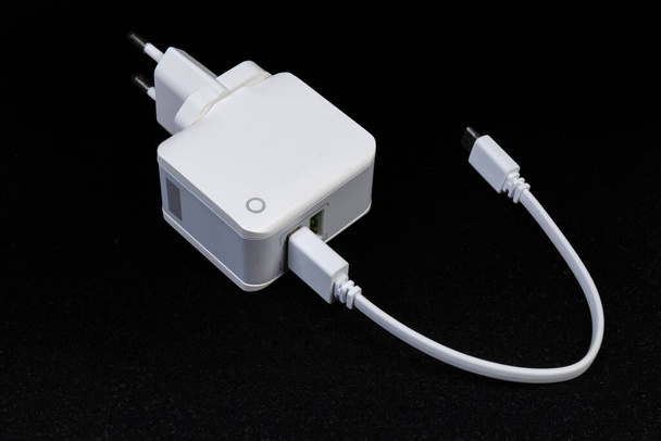 AC adapter mobil készülékekhez akkumulátorok töltéséhez csatlakoztatott USB kábellel sötét alapon - Fotó, kép