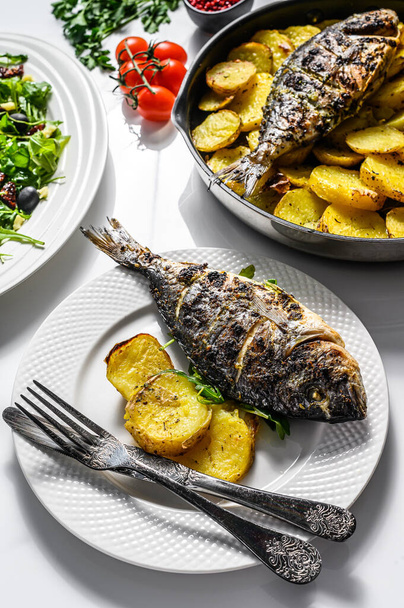 Dinner with grilled sea bream fish, arugula salad with tomatoes, baked potatoes. White background. top view. - Фото, зображення